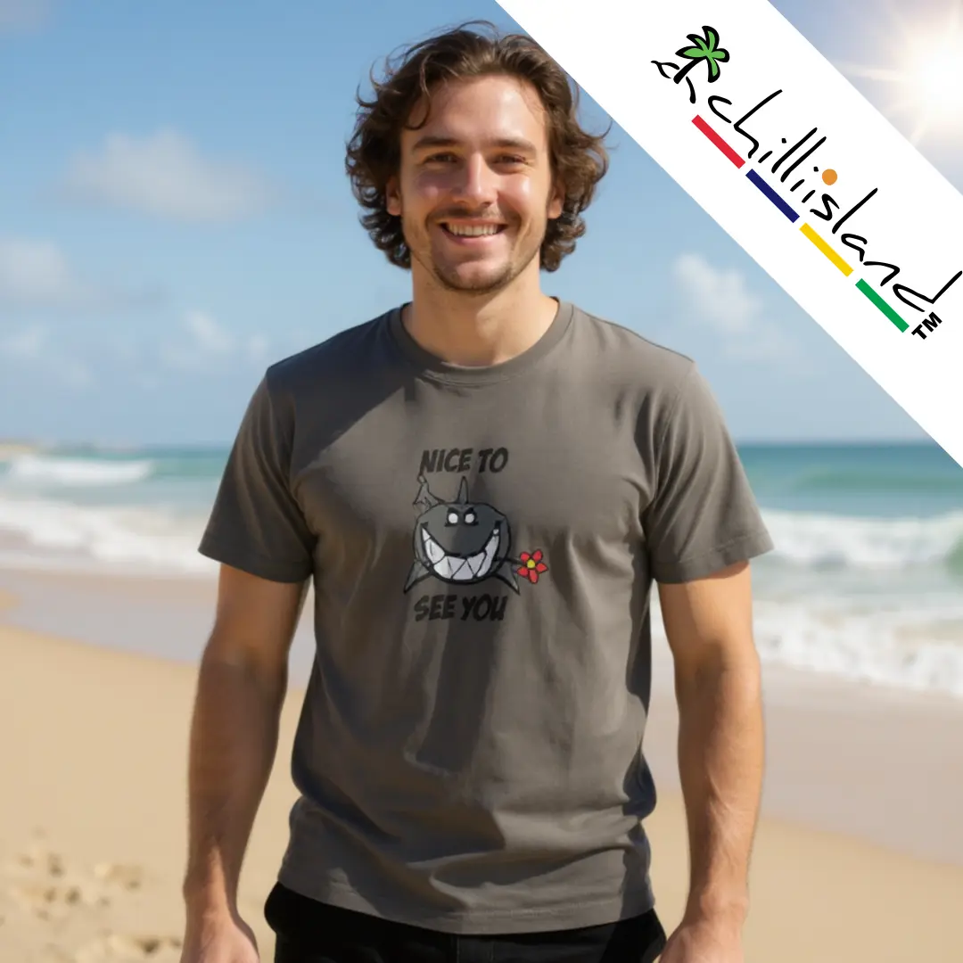 Smiling man on a beach wears a gray Chilliisland T-shirt with a cartoon shark and "Nice to See You" text. Logo "Chillisland" at the top right. Relaxed, sunny vibe.