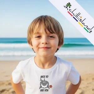 A child in a white Chilliisland T-shirt with a shark graphic stands on a beach, enjoying the ocean time.