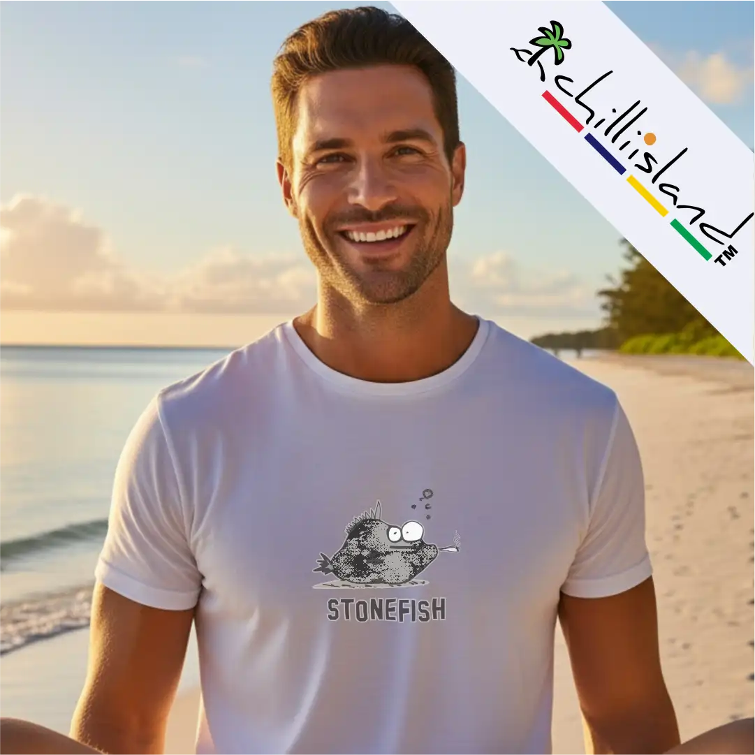A person on a beach wears a white Chilliisland t-shirt featuring a cartoon "stonefish2 design, with a scenic ocean background and evening sky.